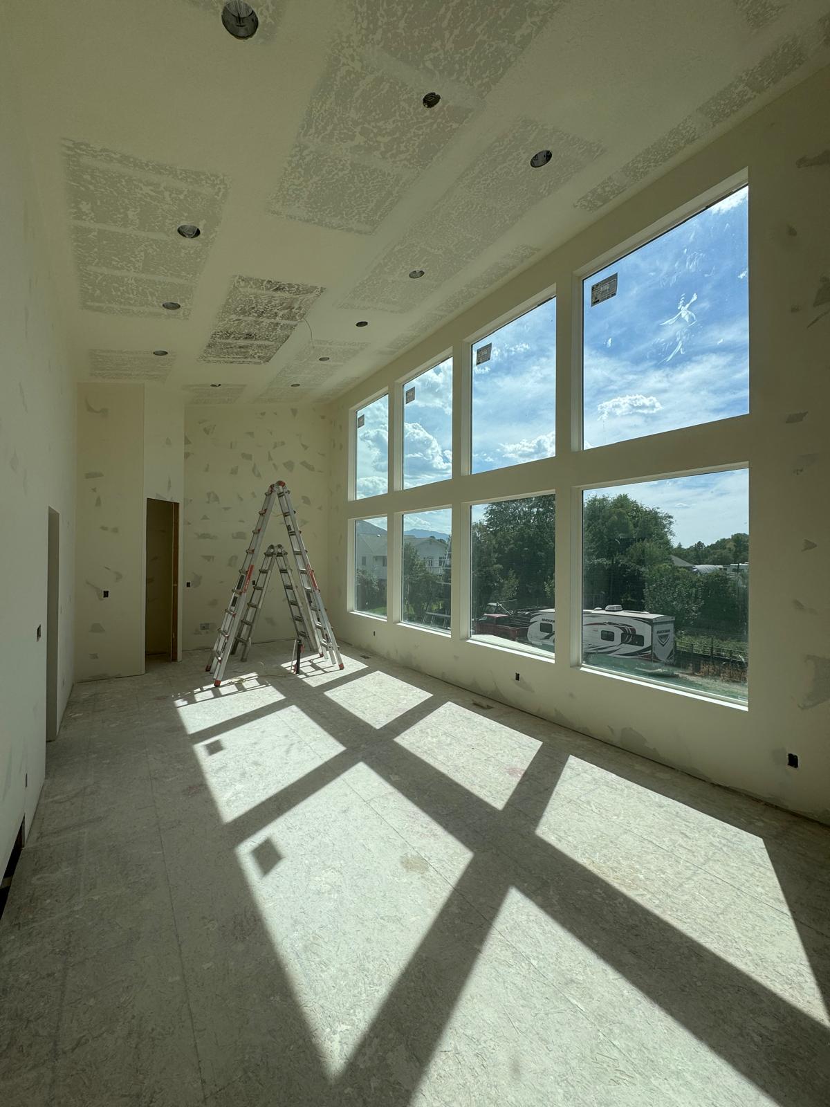 Drywall repair in progress — bright room with ladder and large windows