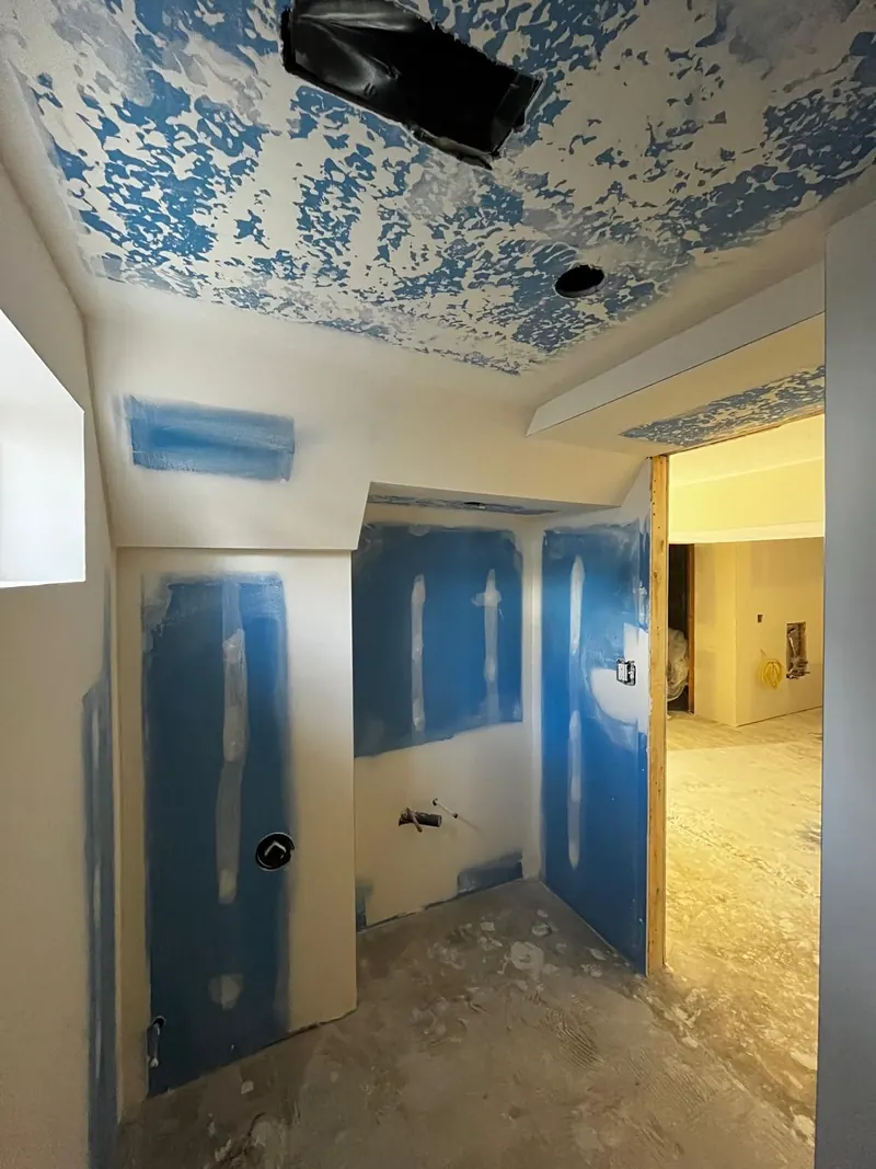 Basement bathroom walls hung in blue moisture-resistant drywall, seams taped and the ceiling textured