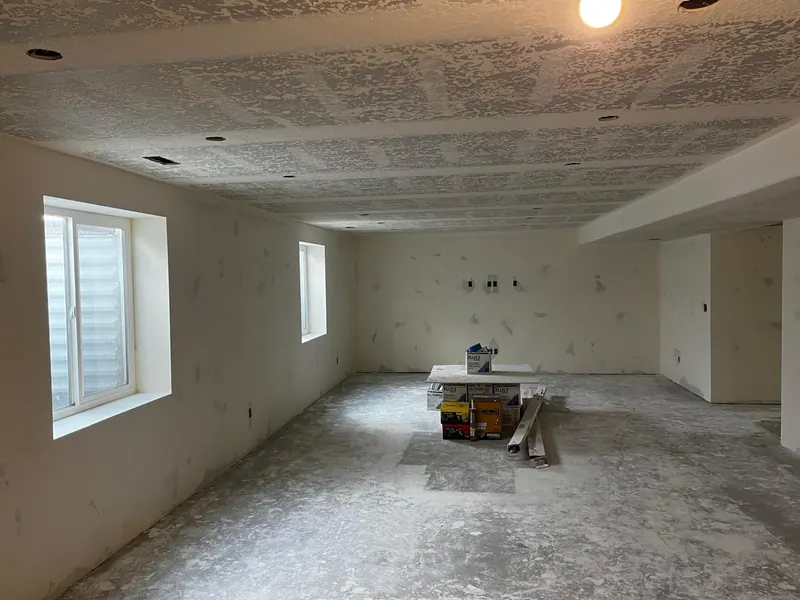 Basement drywall ready for paint, with joint compound and supplies stacked in the middle of the room
