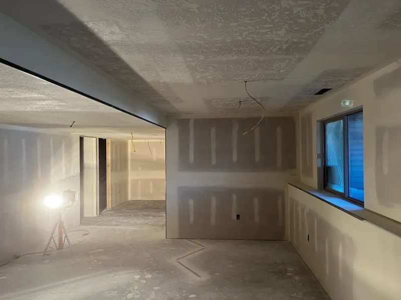Basement living area with drywall taped and mudded, a knockdown ceiling and a work light on a stand