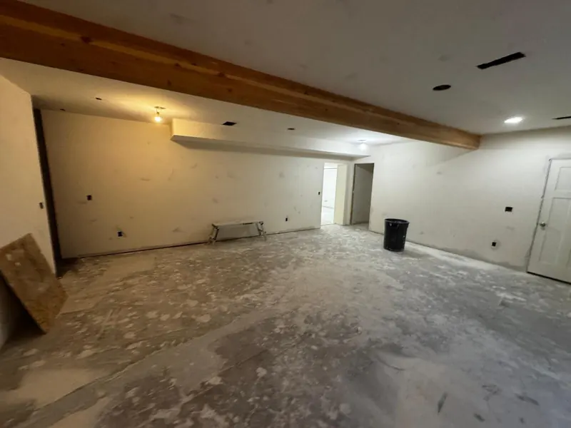 Basement drywall finished around an exposed wood beam, walls ready for paint