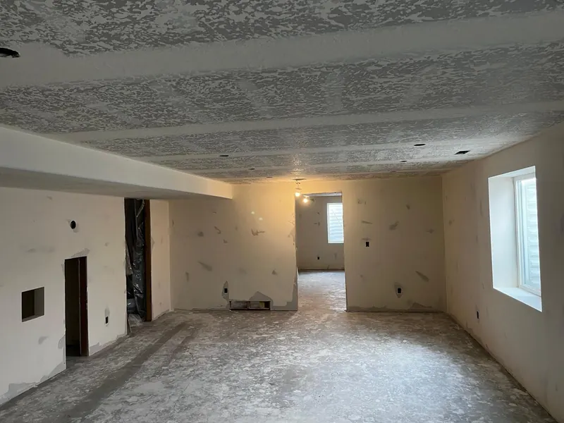 Large basement room with a knockdown ceiling, drywall window returns and walls ready for paint