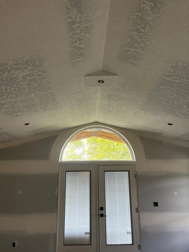Vaulted ceiling finished with knockdown texture above an arched window and double doors